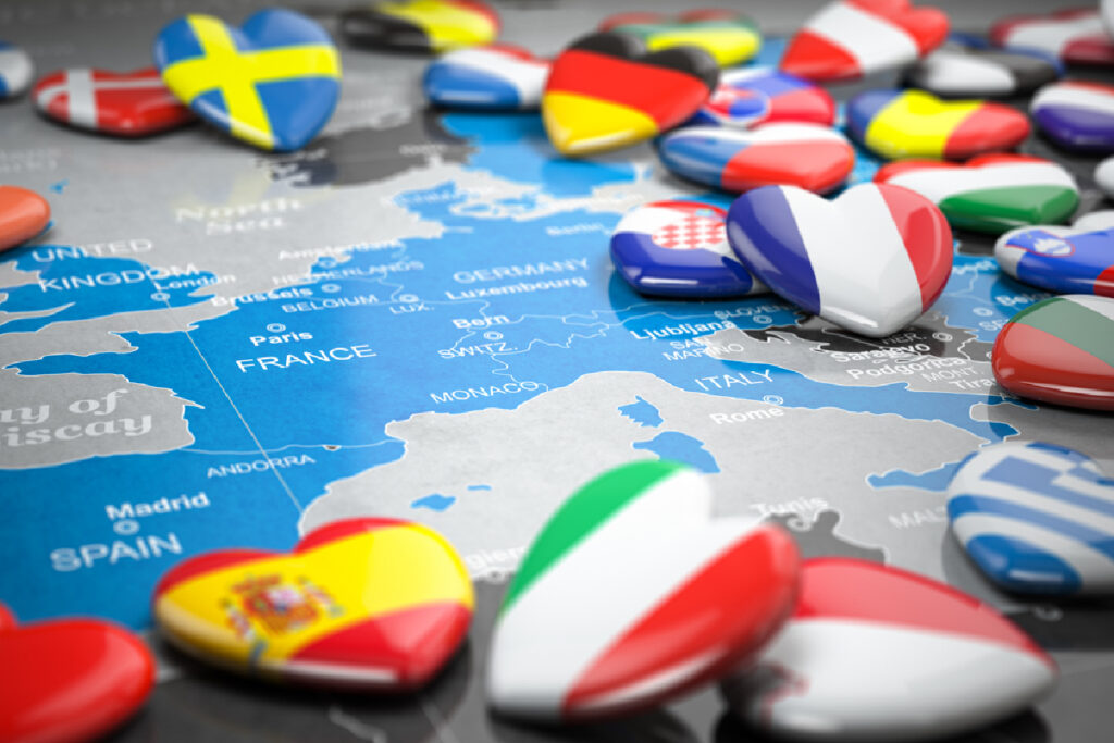 Heart-shaped badges with various European country flags are scattered on a map of Europe. The colorful badges convey a sense of unity and diversity.